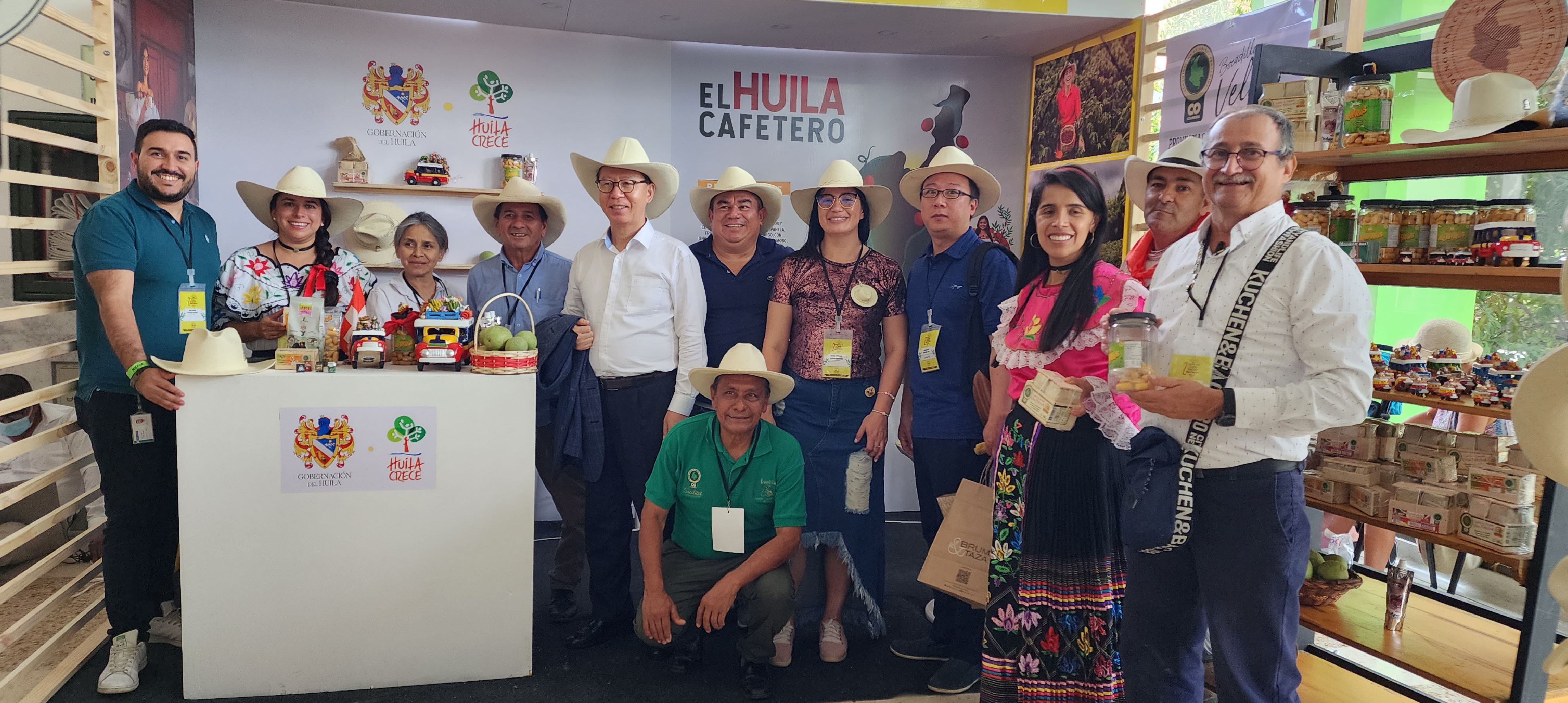 Asistentes al evento sonríen y miran la cámara, parados al lado del stand con productos de denominación de origen de Santander y Huila, en el marco del Col-Col realizado.