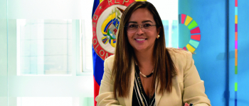 La directora de APC-Colombia, Viviana Manrique Zuluaga Firmando el documento, detrás de ella la bandera de Colombia