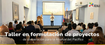 Personas reunidas en un auditorio en donde hay una persona exponiendo en la tarima sobre taller en formulación de proyectos de cooperación para Alianza del Pacífico. 